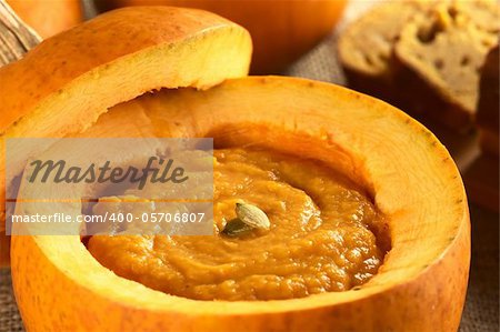 Fresh creamy pumpkin soup served in a pumpkin and garnished with pumpkin seeds (Selective Focus, Focus on the seeds)