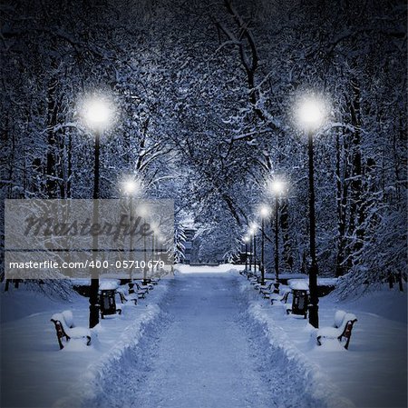 Winter park in the evening covered with snow with a row of lamps