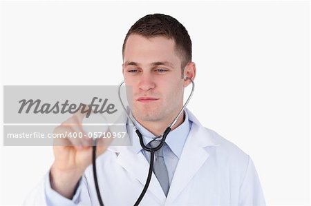 Close up of doctor looking at his stethoscope while using it on white background