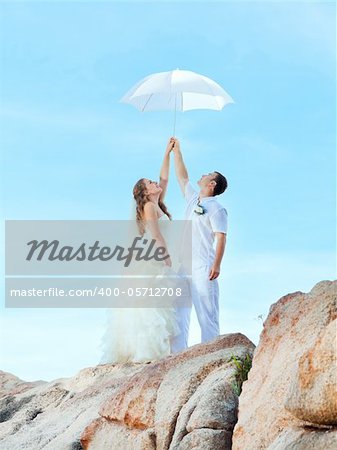 Bride and groom holding an umbrella on a rock.