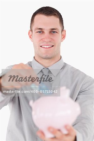 Portrait of a young businessman putting a twenty euros note in a piggy bank against a white background