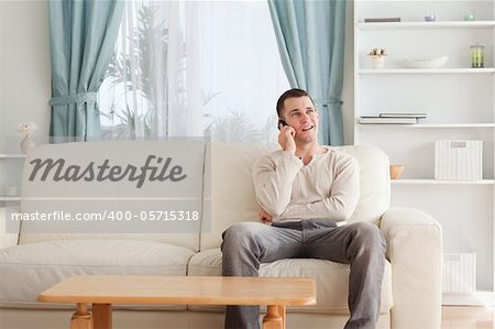 Man on the phone while sitting on his sofa against a white background
