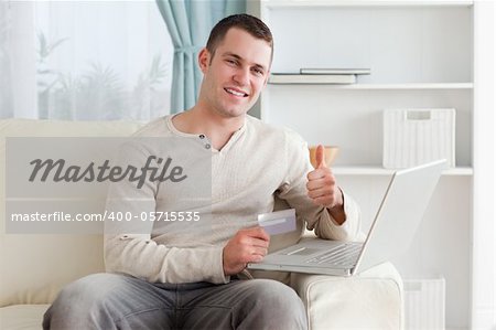 Happy man shopping online with the thumb up in his living room