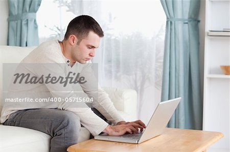 Young man typing on his laptop in his living room