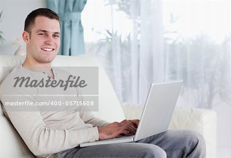 Happy man typing on his notebook in his living room