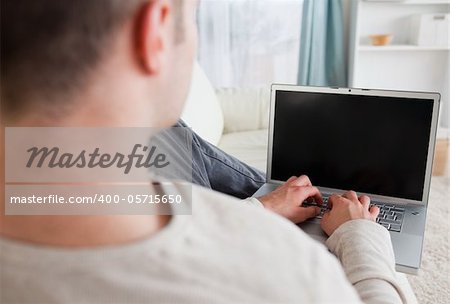 Man lying on his couch while using a laptop in his living room