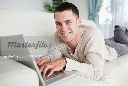 Smiling man lying on a couch with a laptop while looking at the camera