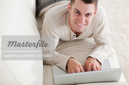 Happy man lying on a couch with a notebook in his living room