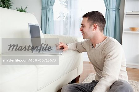 Smiling man sitting on a carpet while using a laptop in his living room