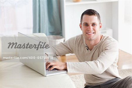 Smiling man sitting on a carpet posing with a notebook in his living room