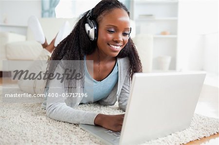 Smiling woman lying on floor with her notebook listening to music