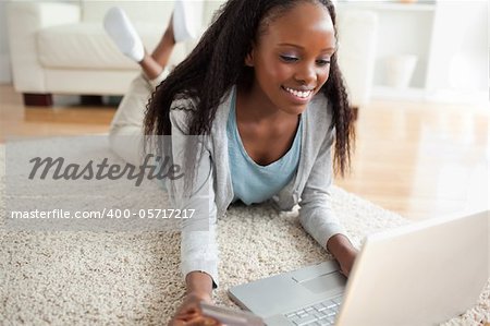 Close up of smiling woman lying on the floor with her laptop shopping online