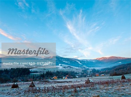 first autumn frosts on pasture with haystacks and sunrise in the mountains village