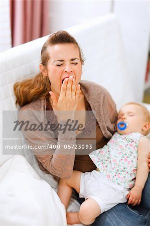 Young mother with sleeping baby on hands yawing at home