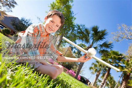 A young boy sitting on grass outside playing with a toy model airplane