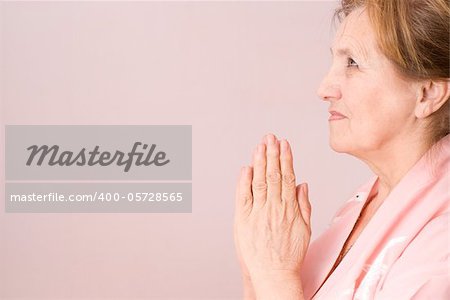 elderly woman praying on a pink background