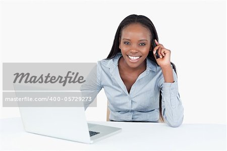 Businesswoman making a phone call while using a laptop against a white background
