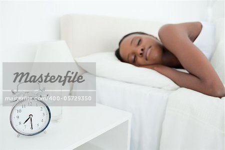 Woman sleeping while her alarm clock is ringing in her bedroom