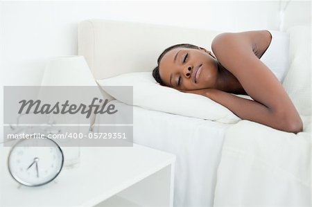 Young woman sleeping while her alarm clock is ringing in her bedroom