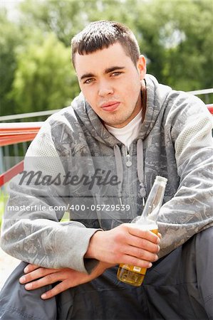 Young Man Sitting In Playground Drinking Beer