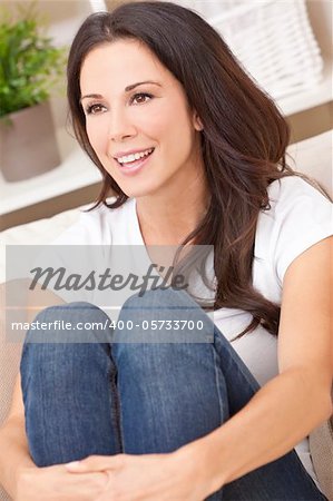 Portrait of a beautiful brunette young woman in jeans and t-shirt smiling siting on her sofa at home