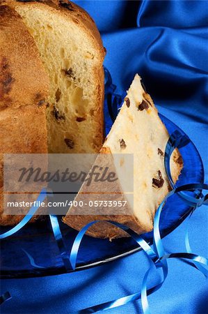 Panettone the italian Christmas fruit cake served on a blue glass plate over a blue fabric background. Selective focus.