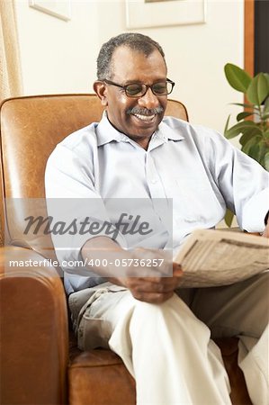 Senior Man Sitting In Armchair Reading Newspaper