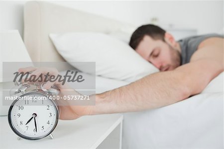 Sleeping young man being awakened by an alarm clock in his bedroom