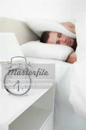 Portrait of a unhappy young man covering his ears with a pillow while his alarm clock is ringing