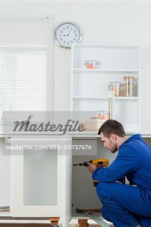 Portrait of a handsome handyman fixing a door in a kitchen
