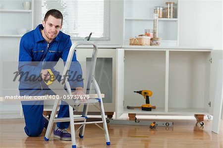 Smiling handyman cutting a wooden board in a kitchen