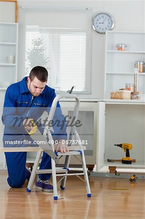 Portrait of a young handyman cutting a wooden board in a kitchen