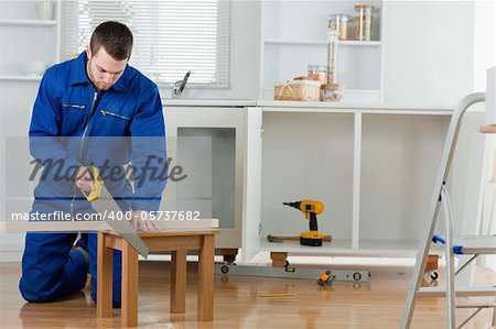 Young handyman cutting a wooden board in a kitchen