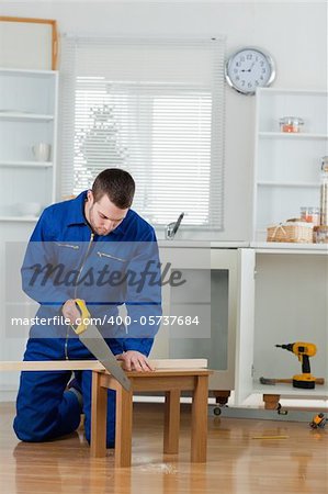 Portrait of a handsome handyman cutting a wooden board in a kitchen