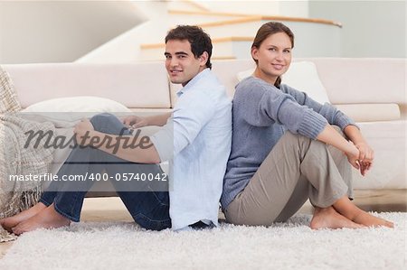 Young couple sitting back to back in their living room