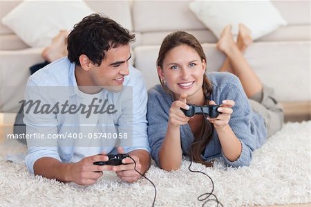 Lovely couple playing video games while lying on a carpet