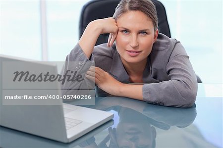 Beautiful businesswoman leaning on her desk while looking at the camera