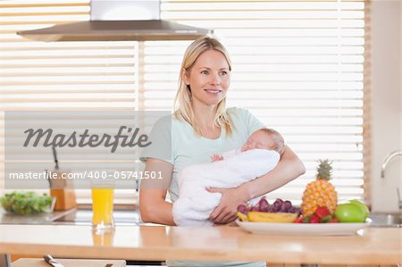 Young woman standing in the kitchen holding her baby
