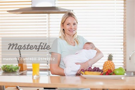 Smiling woman standing in the kitchen while holding her baby