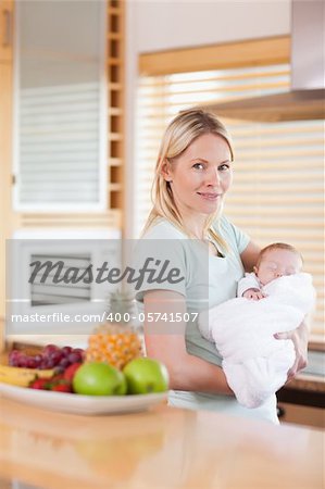 Side view of woman standing in the kitchen with her baby on her arms
