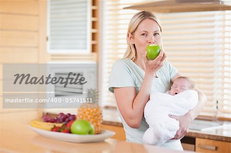 Young woman enjoying an apple with her baby on her arms