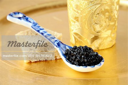 Black caviar in spoon on gold background