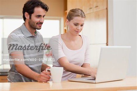 Couple using a laptop while having coffee in their kitchen