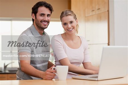 Smiling couple using a notebook while having coffee in their kitchen