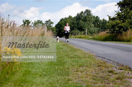 Sporty woman and dog jogging along a road in summertime