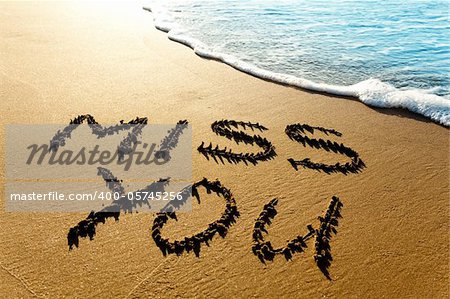 Dramatic inscription "Miss You" on wet golden beach sand in sunset light