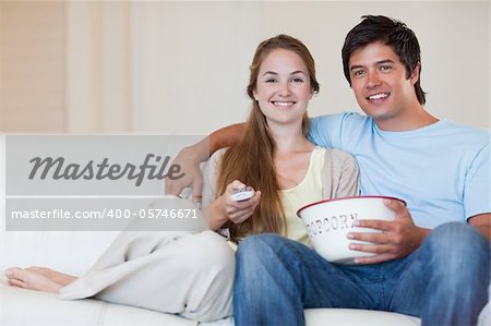 Young couple watching television while eating popcorn in their living room