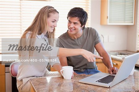 Smiling couple having coffee while using a notebook in their kitchen