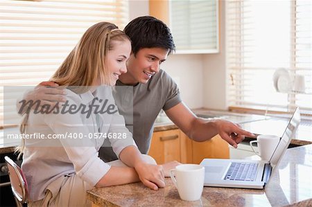 Couple having coffee while using a laptop in their kitchen