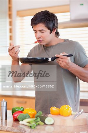 Portrait of a young man tasting his meal in his kitchen